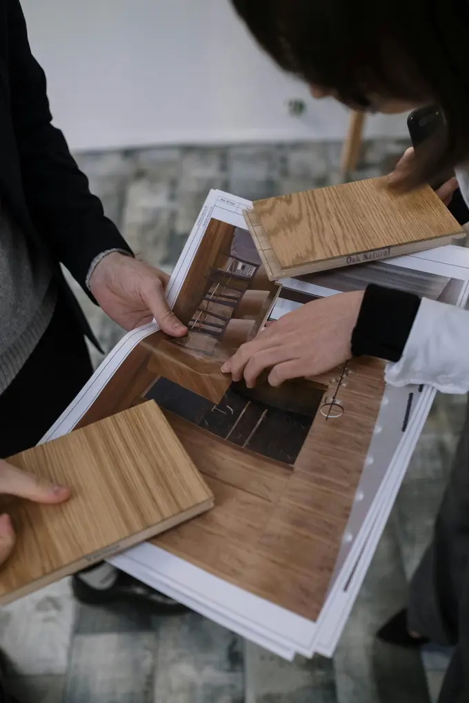 Two people comparing wood samples on an open catalogue, reviewing different finishes and tones