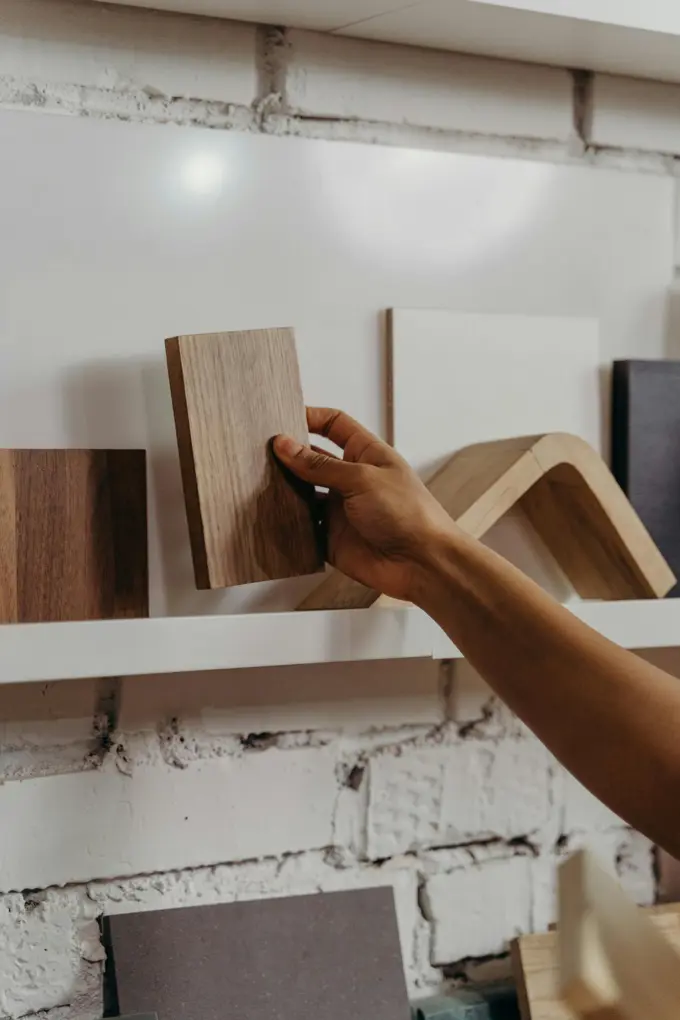 Hand selecting a wood sample from a shelf, among several blocks with different tones and finishes.