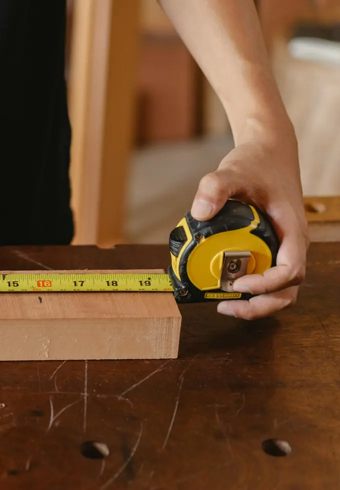 Hand measuring a wooden block with a tape measure on a wooden workbench.